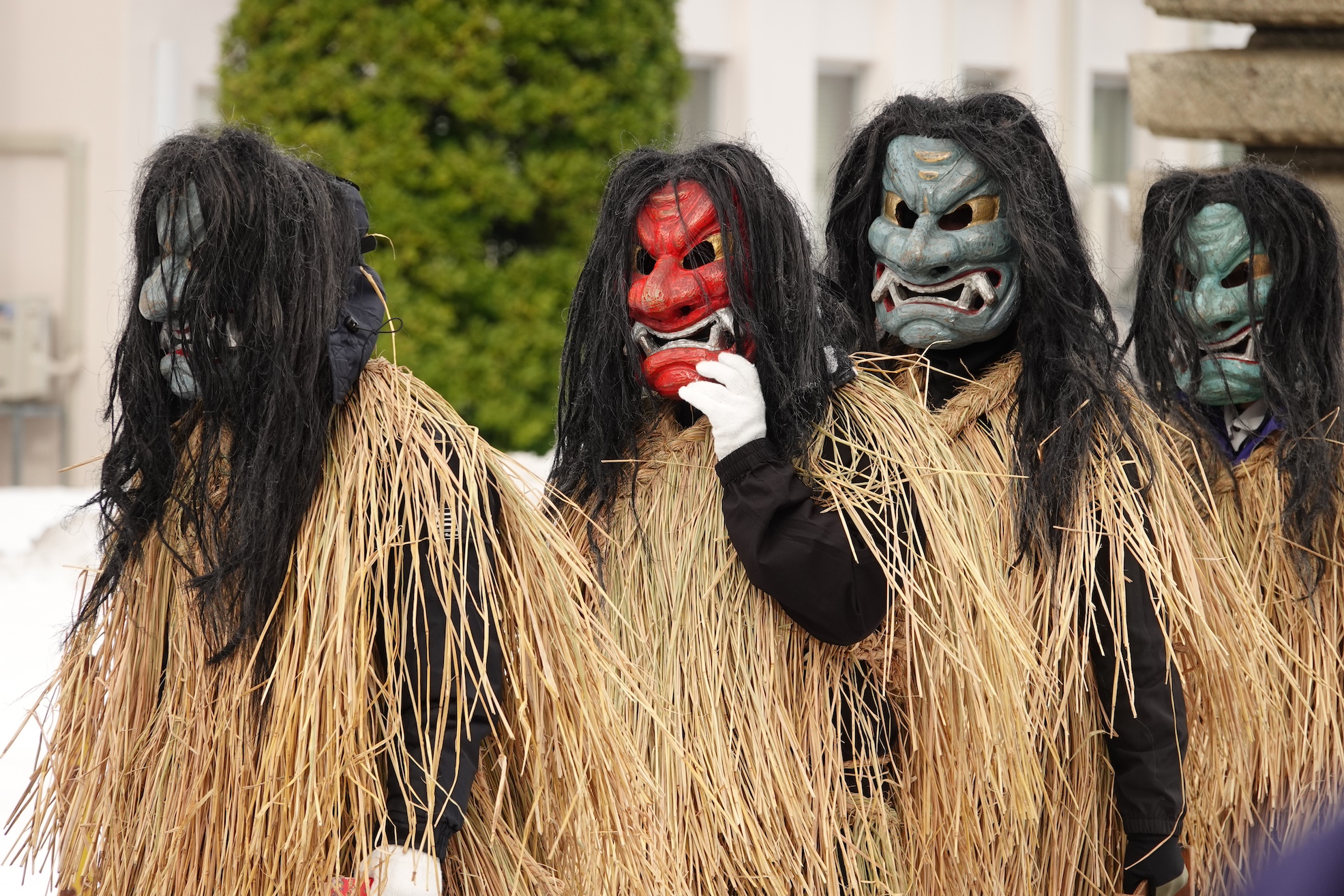 Four young men in Namahage masks walking--three have green masks, one has a red mask.
