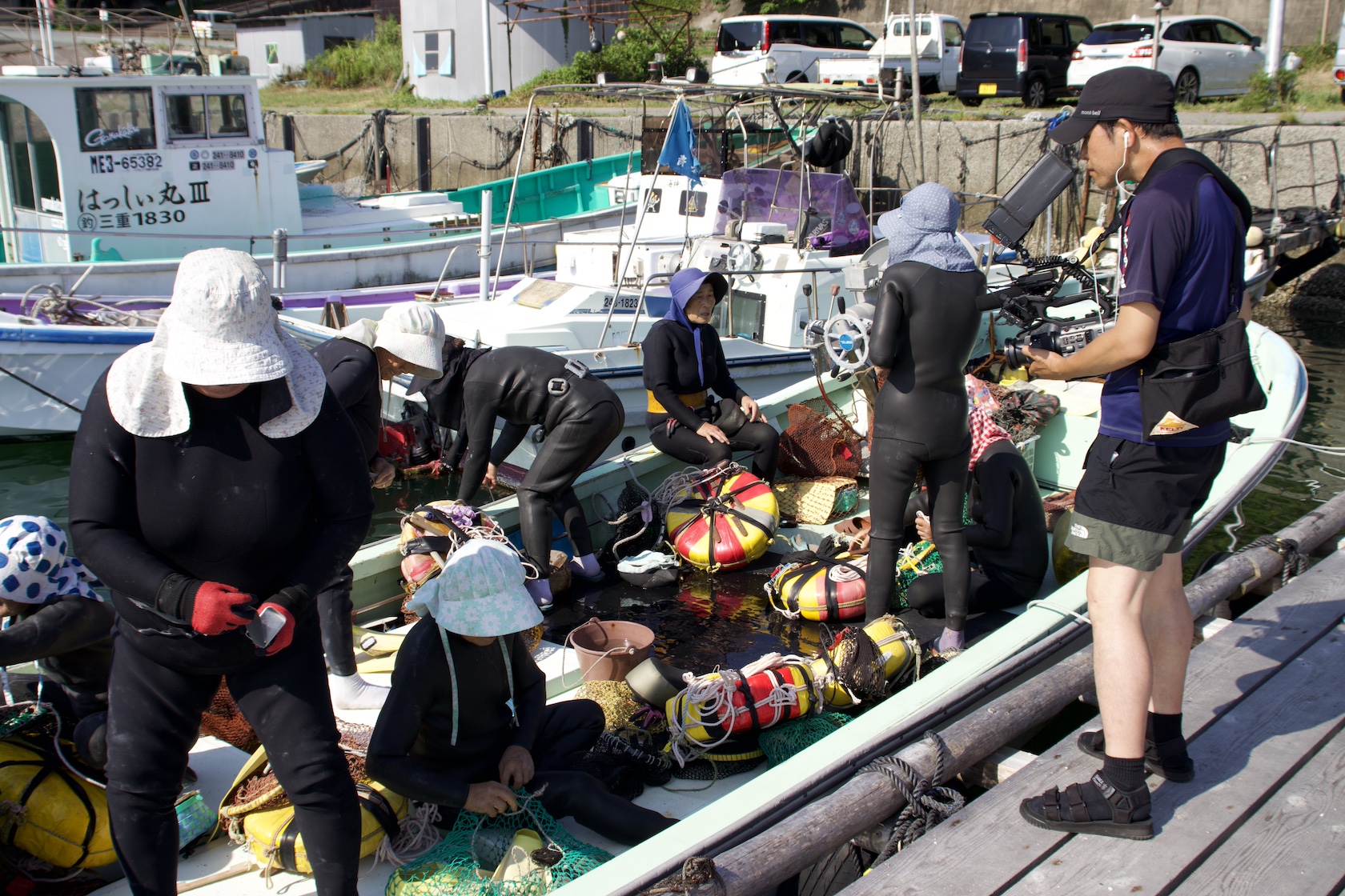 A group of ama (female divers) prepare their boat as a TV crew member films.