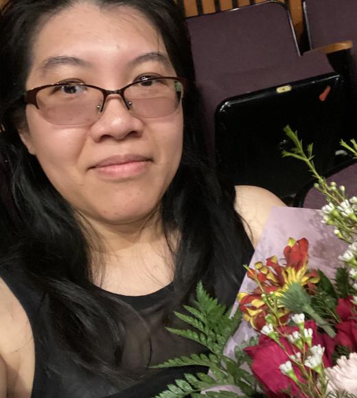 A photo of a woman wearing glasses holding flowers.