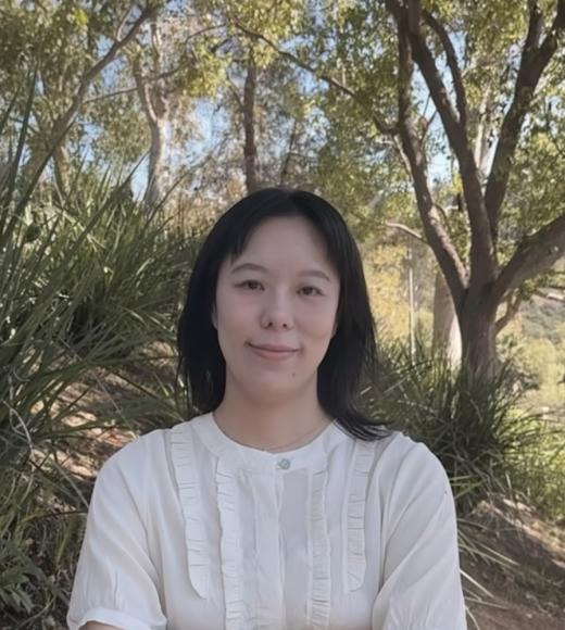 Woman in white shirt standing in front of trees