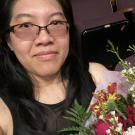 A photo of a woman wearing glasses holding flowers.